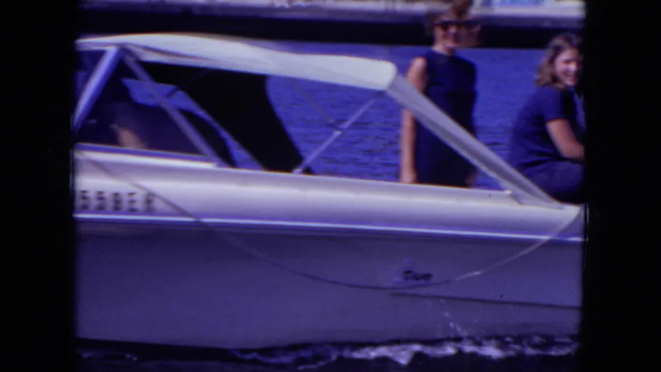 Two young people in dark casual clothing ride in a white speed boat on a Mississippi lake, with wake visible along the hull.