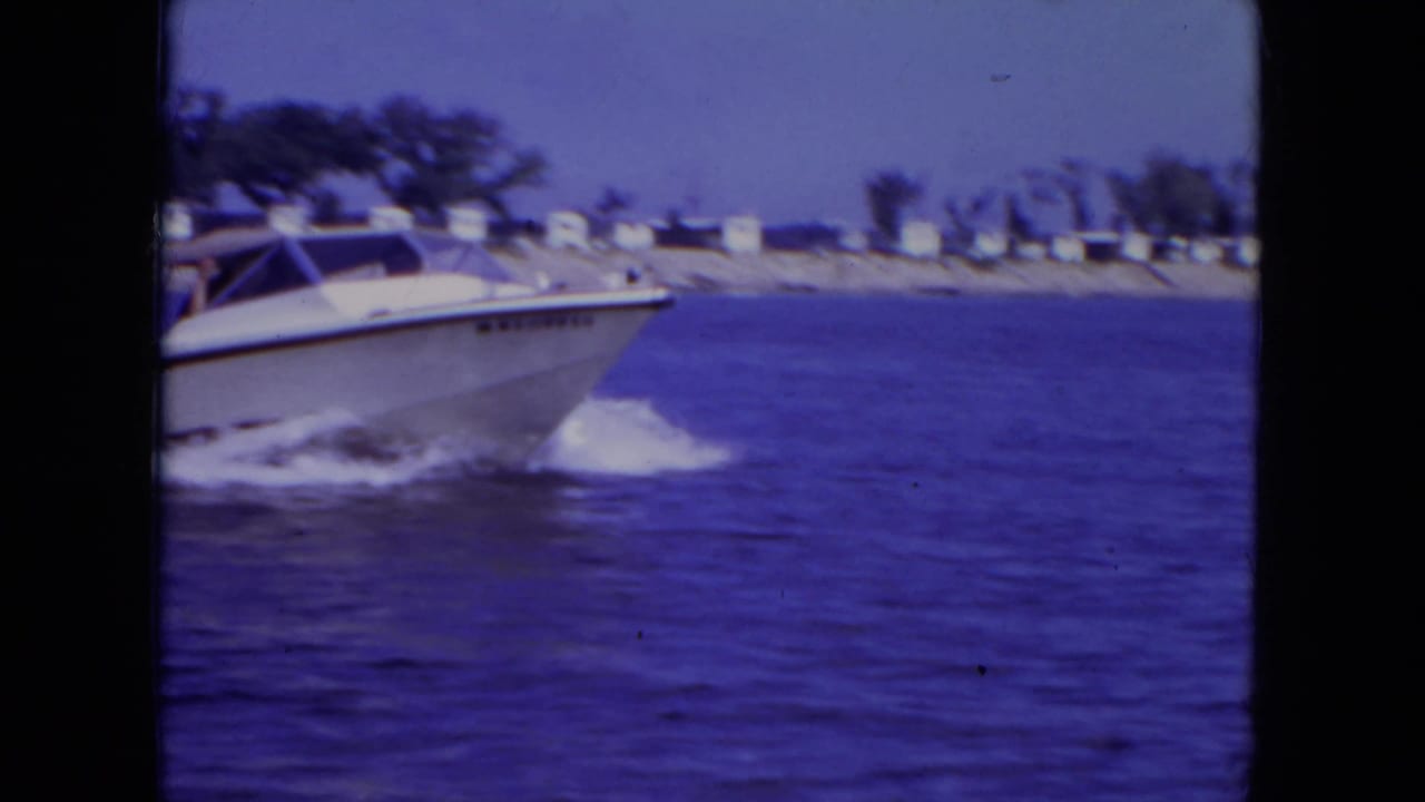 1971 Mississippi 8mm frame showing a white speedboat crossing open water with shore trees in the distance.