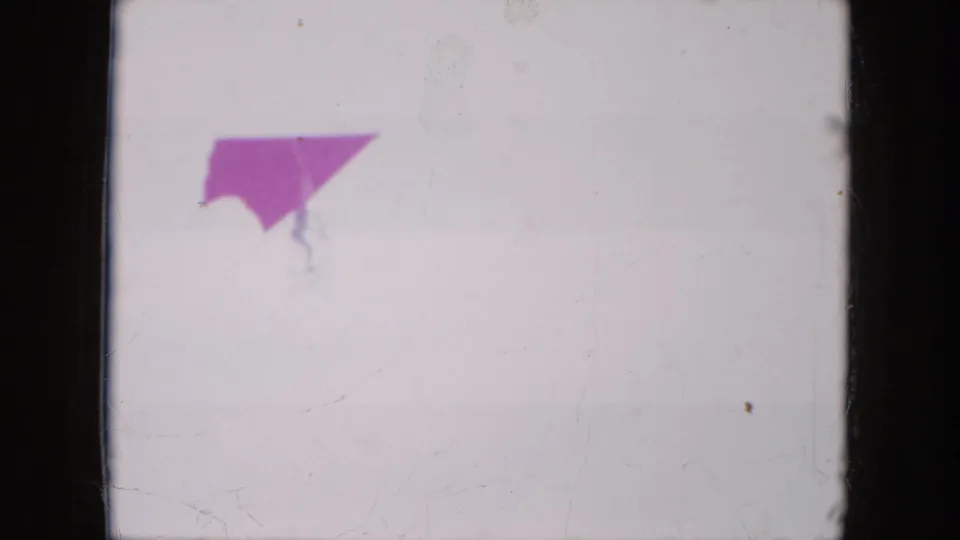 A red hang glider wing appears high in a pale sky in 1971 Mississippi 8mm footage, with the pilot barely visible below.