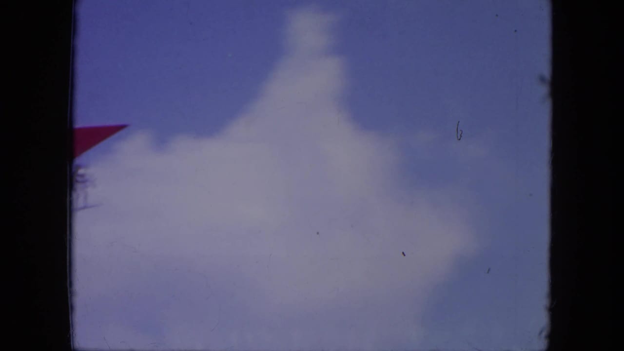 Partly cloudy blue sky with a small red hang glider at the left edge.