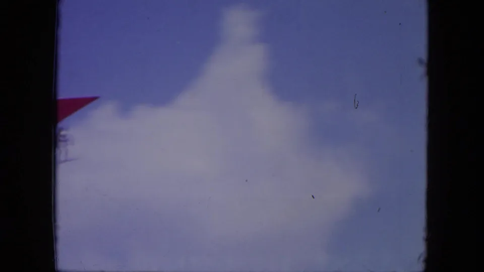 A small red hang glider crosses the edge of a blue, partly cloudy sky in the Mississippi 1971 home-movie footage.