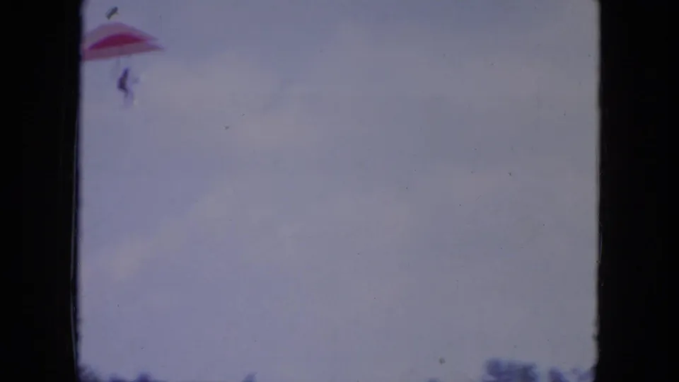 A distant person under a red hang glider appears near the top of a pale Mississippi sky in 1971 8mm footage.