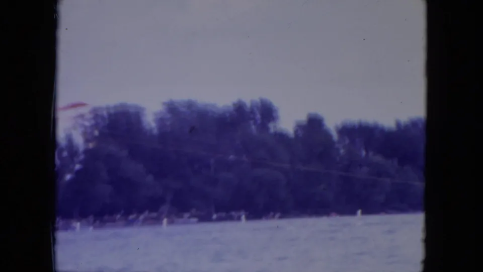 A wooded lakeshore fills the lower frame as the red hang glider slips partly out of view at the left edge.