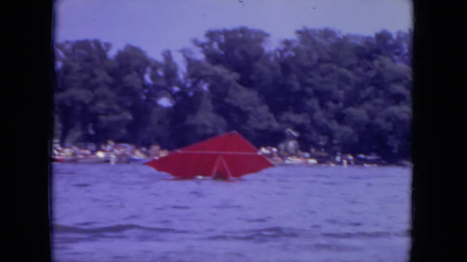 A closer 1971 Mississippi lake view shows the red parasail spread across the water, with trees and small figures visible along the shore.