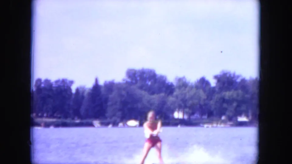 A young woman appears to water ski across a Mississippi lake in 1971, holding a tow line as white spray trails behind her near the wooded shore.