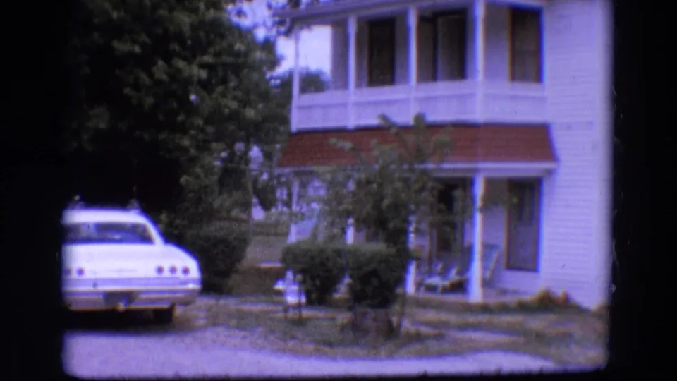 1968 Diller, Nebraska frame with a white car in a driveway before a porch-fronted clapboard house and yard plantings.