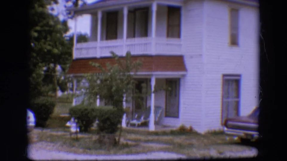 1968 Diller, Nebraska home exterior showing porch railings, front yard shrubs, and a partial parked car at the curb or driveway edge.
