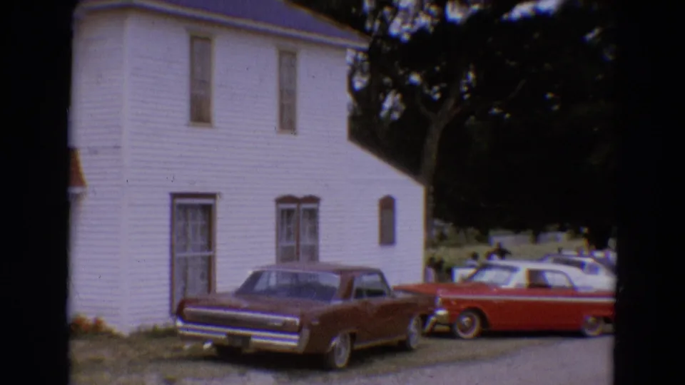 A 1968 home-movie frame shows the house side, maroon sedan, red convertible, and additional parked cars under trees.
