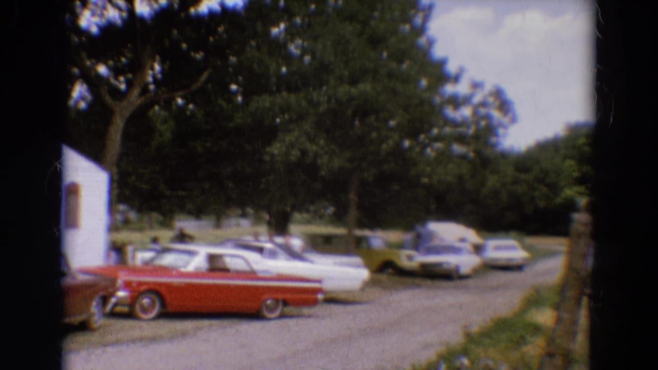 Red and white parked cars on a gravel drive with trees and a building edge visible.