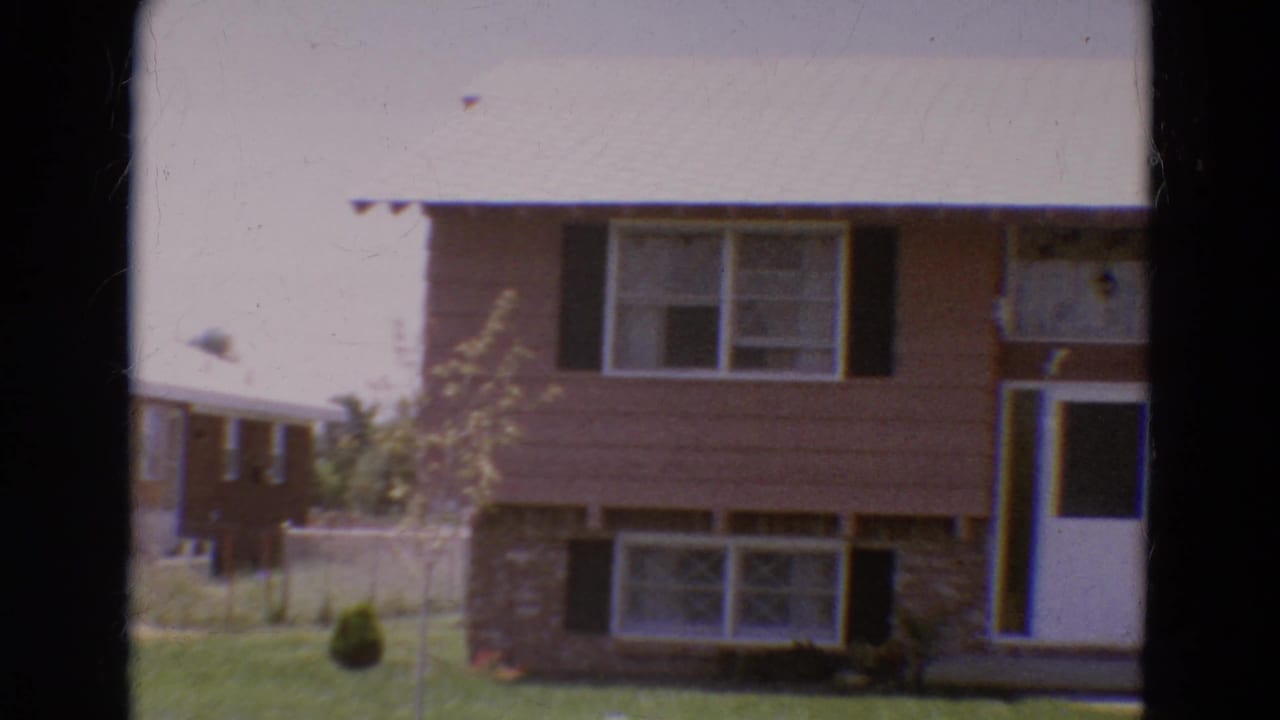 Split-level house with brown siding, brick lower level, black shutters, white roof, and lawn.