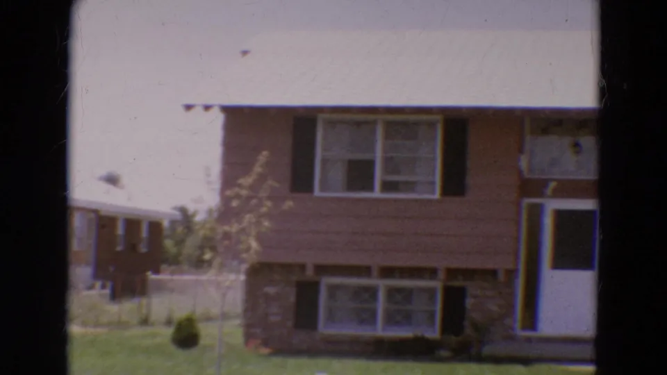 1968 Diller, Nebraska home-movie frame showing a split-level residential exterior with brown siding, brickwork, black shutters, and a pale roof.
