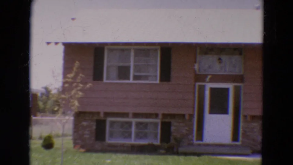 1968 Diller, Nebraska frame of the house front, showing a white door, upper and lower windows, black shutters, and a grassy yard.