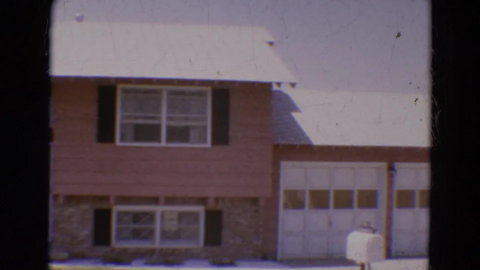 1968 Diller, Nebraska frame with the home centered on shuttered upper windows, stone lower facing, white garage door, and mailbox.