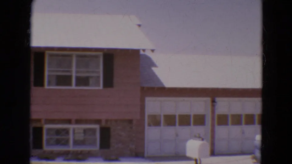 1968 Diller, Nebraska home-movie frame showing the pan moving right across the house facade, garage doors, and mailbox.