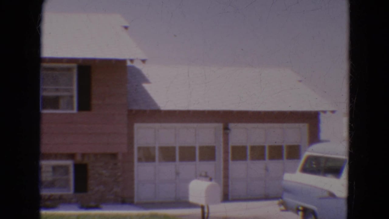 1968 Diller, Nebraska home-movie frame showing a suburban house facade, white garage doors, front lawn, mailbox, and partial station wagon.