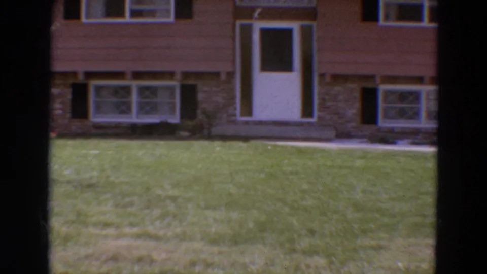 1968 Diller, Nebraska exterior frame showing a closer section of the brown-sided house with white door, front windows, shutters, and lawn.