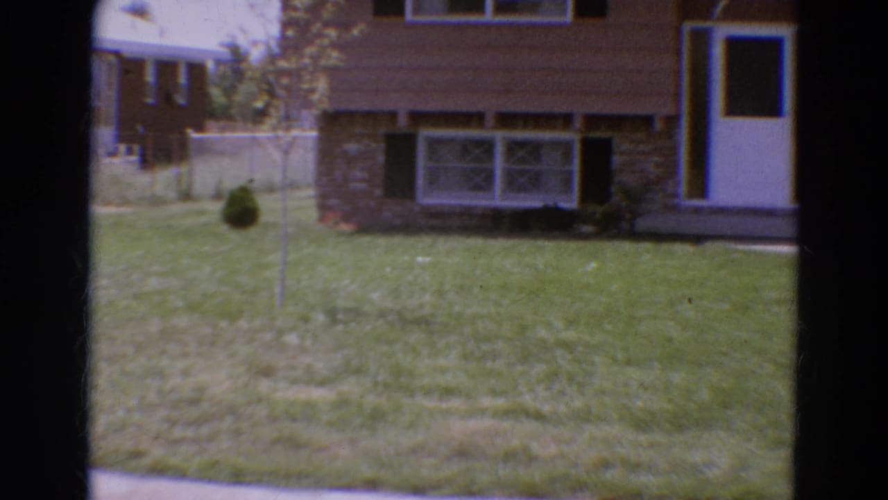 Front yard view of a brown house with white door, windows, and green lawn.