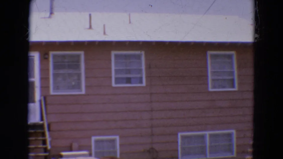 1968 Diller, Nebraska 8mm frame showing white-framed windows, basement windows, brown siding, and part of the exterior steps.