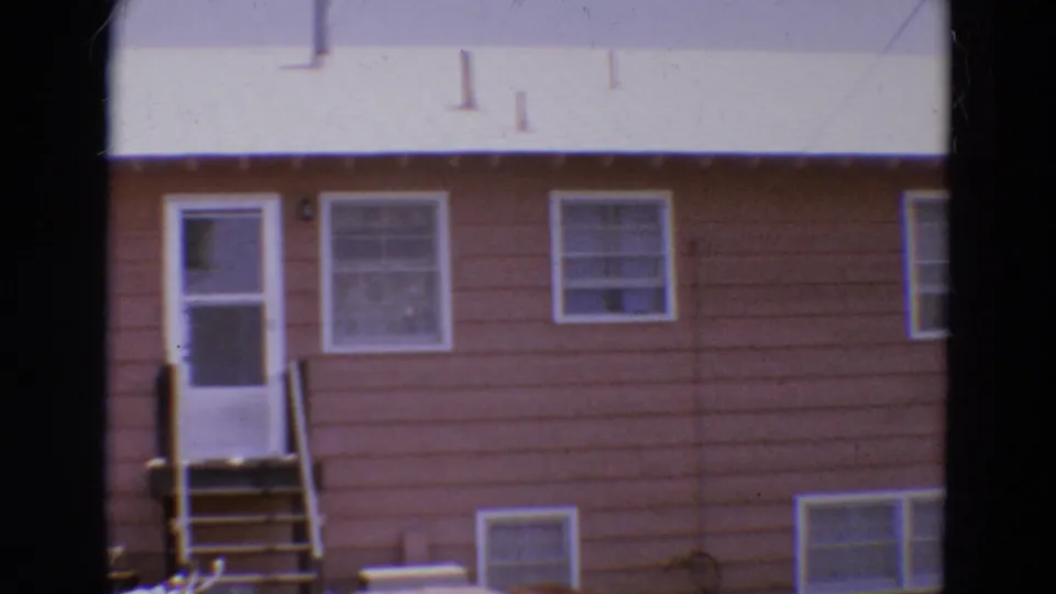 1968 Diller, Nebraska 8mm frame showing a white screen door, small wooden stairs, brown siding, and multiple windows.