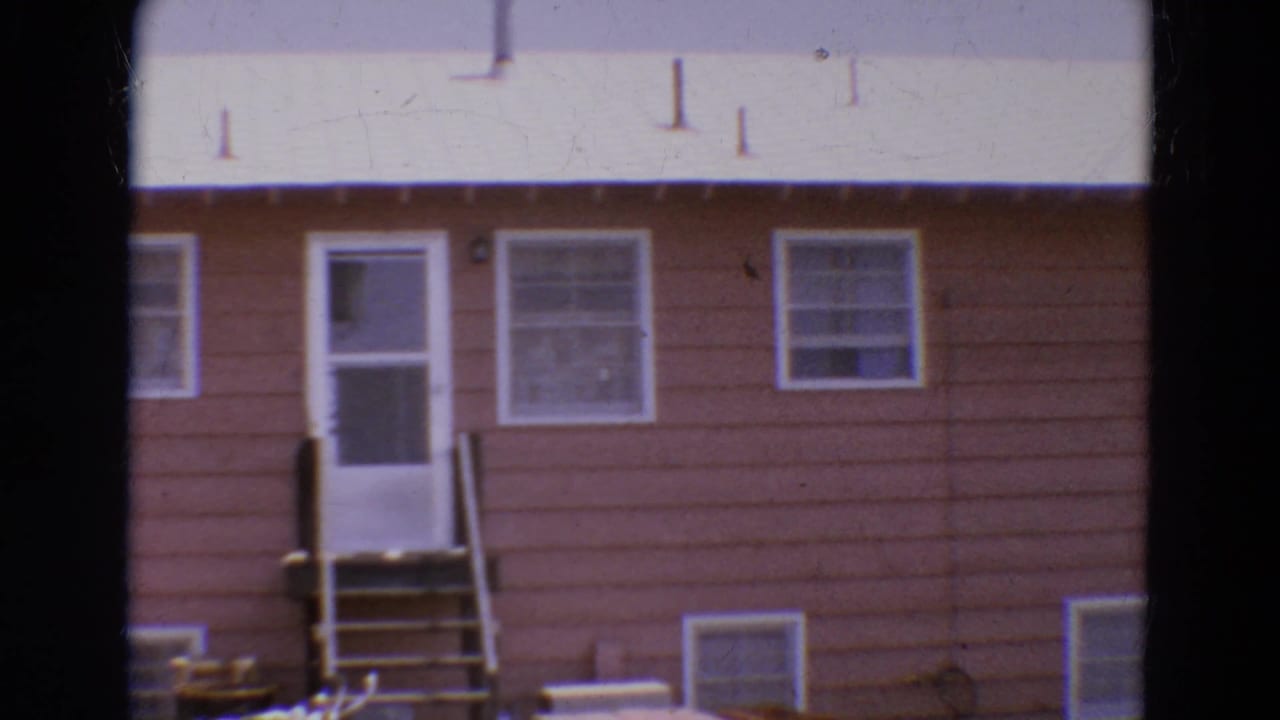 1968 Diller, Nebraska home-movie frame showing a brown house exterior with white door, small steps, windows, and pale roof.