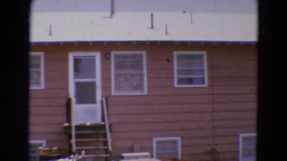 1968 Diller, Nebraska home-movie frame showing a brown house exterior with white door, small steps, windows, and pale roof.