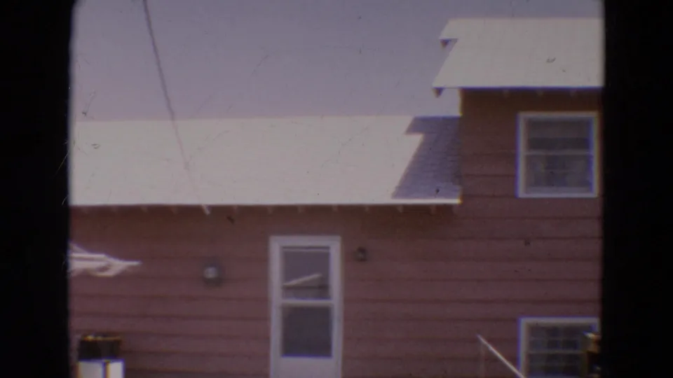 1968 Diller, Nebraska home-movie frame showing the side wall of a pink house with a back door, windows, and part of a clothesline.