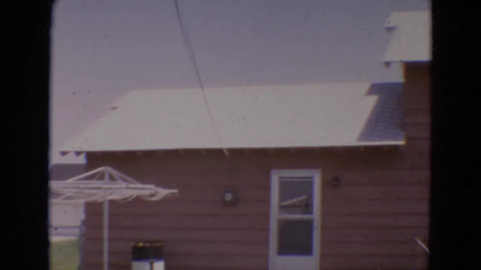 1968 Diller, Nebraska frame showing a backyard clothes drying rack beside a pink house, with a small dog near the lower edge.