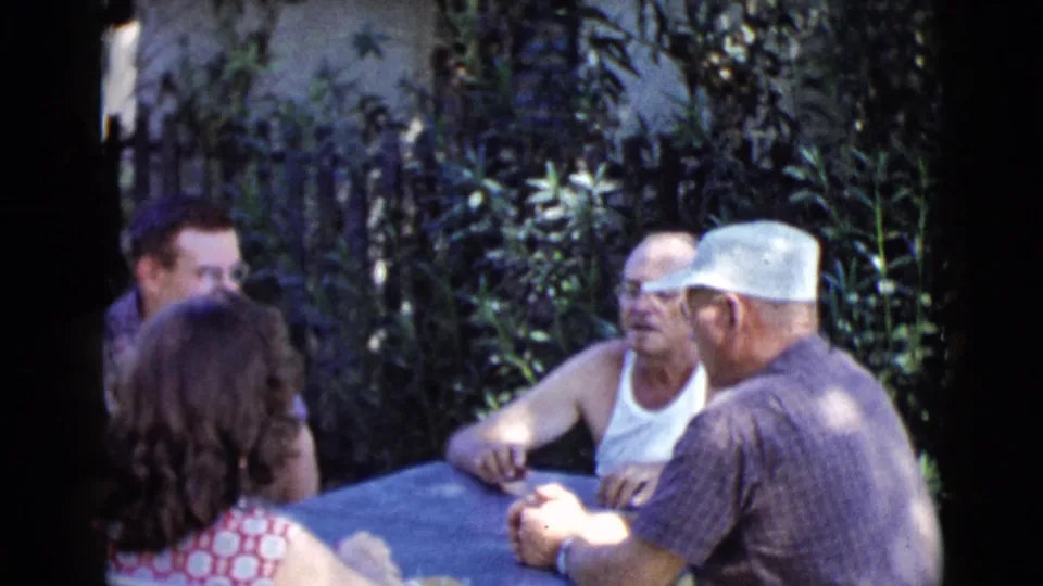 1968 Clarksdale, Arizona home-movie frame showing adults gathered around a blue table in a shaded yard.