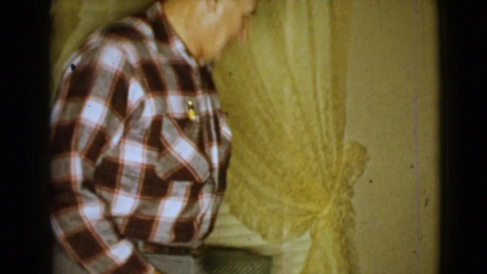 1968 Clarksdale home-movie frame of an older seated man in profile near a yellow curtain and living-room wall.