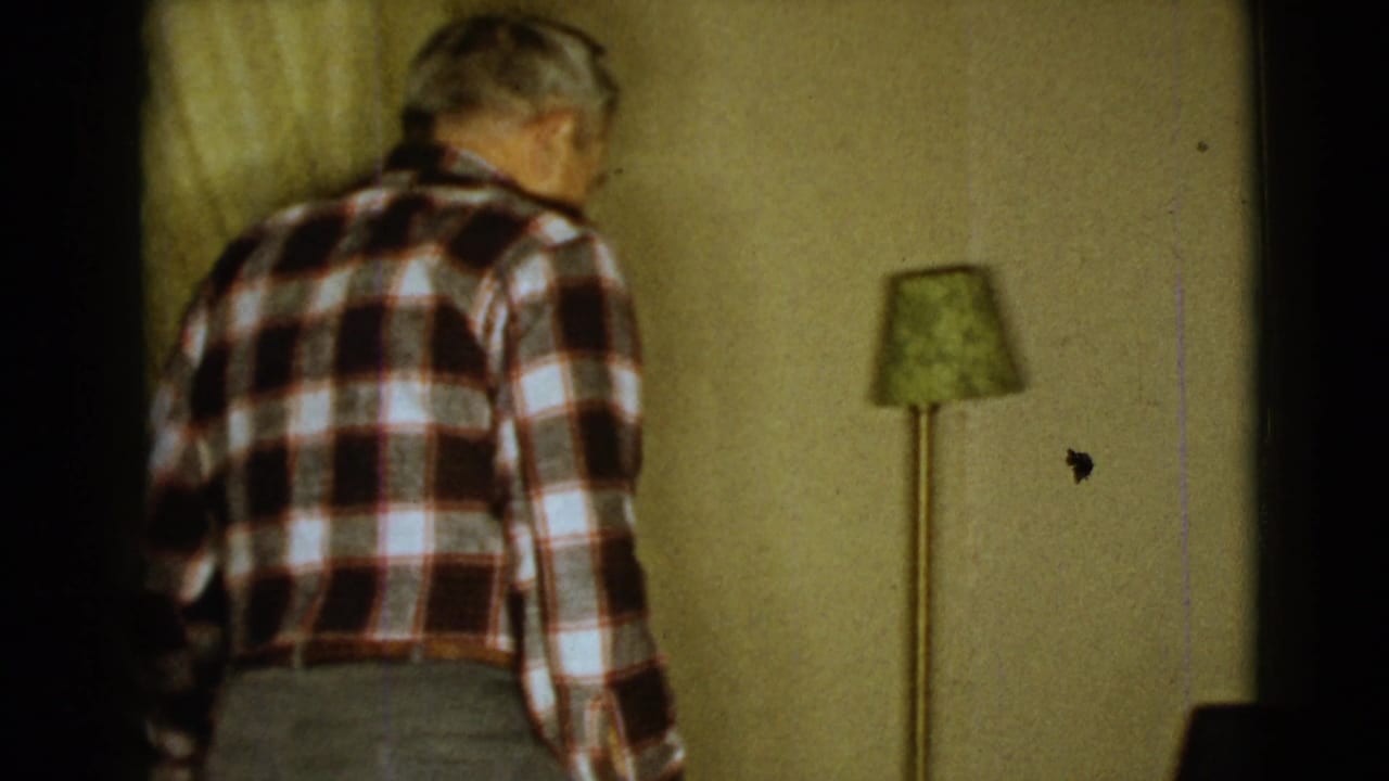 Elderly man seen from behind walking past a floor lamp in a yellow room.