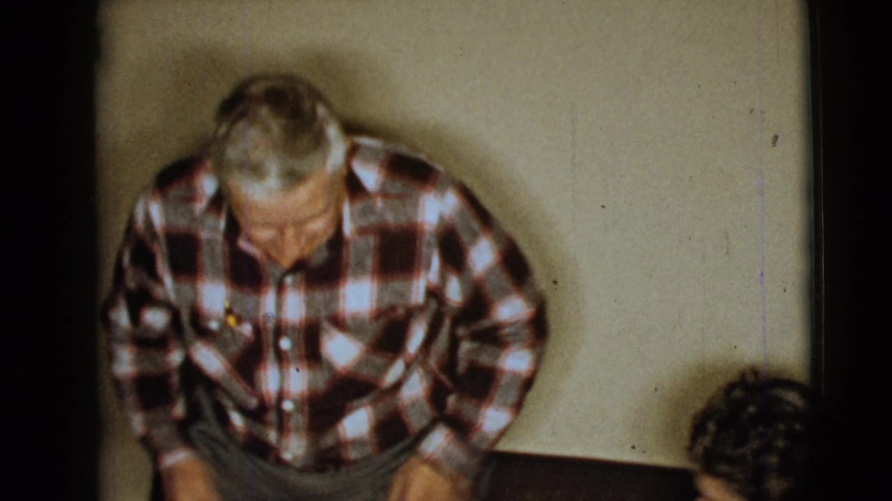 Elderly man in a plaid shirt leans forward in a Clarksdale, Arizona home-movie interior from 1968.