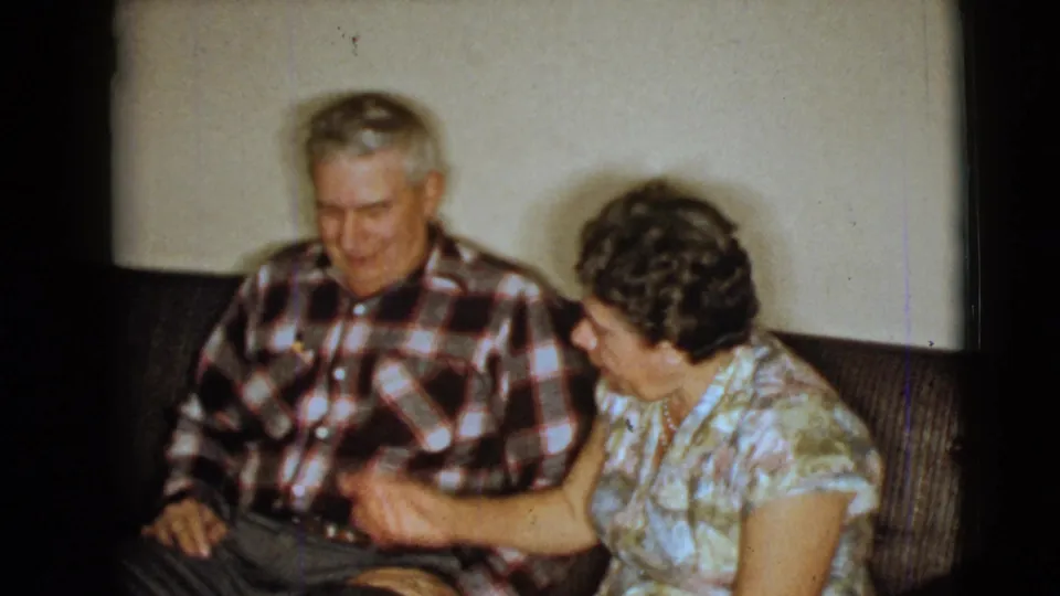 In the 1968 Clarksdale, Arizona home-movie frame, an elderly woman gestures while seated beside a man on a couch.