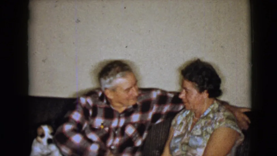 1968 home-movie frame from Clarksdale, Arizona, showing an elderly couple on a couch with a small dog at the left edge.