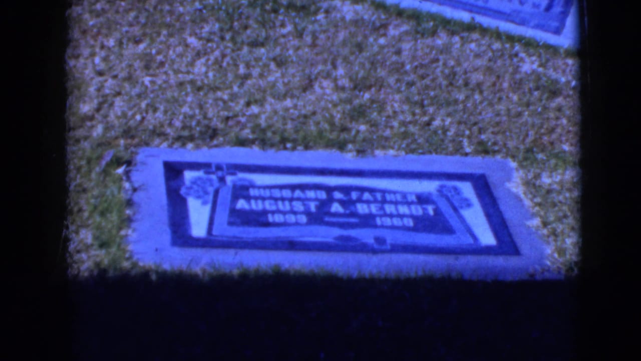 Blue-tinted 8mm frame showing a flat grave marker for August A. Berndt in a grassy cemetery setting.