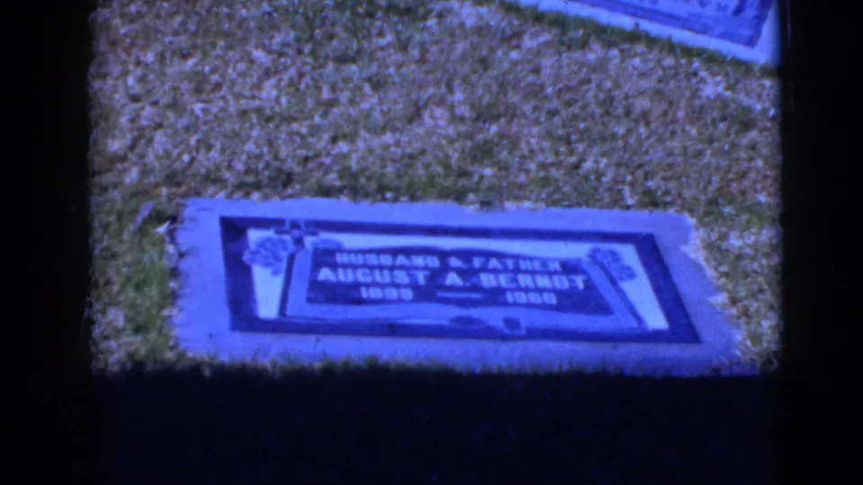 Blue-tinted 8mm frame showing a flat grave marker for August A. Berndt in a grassy cemetery setting.