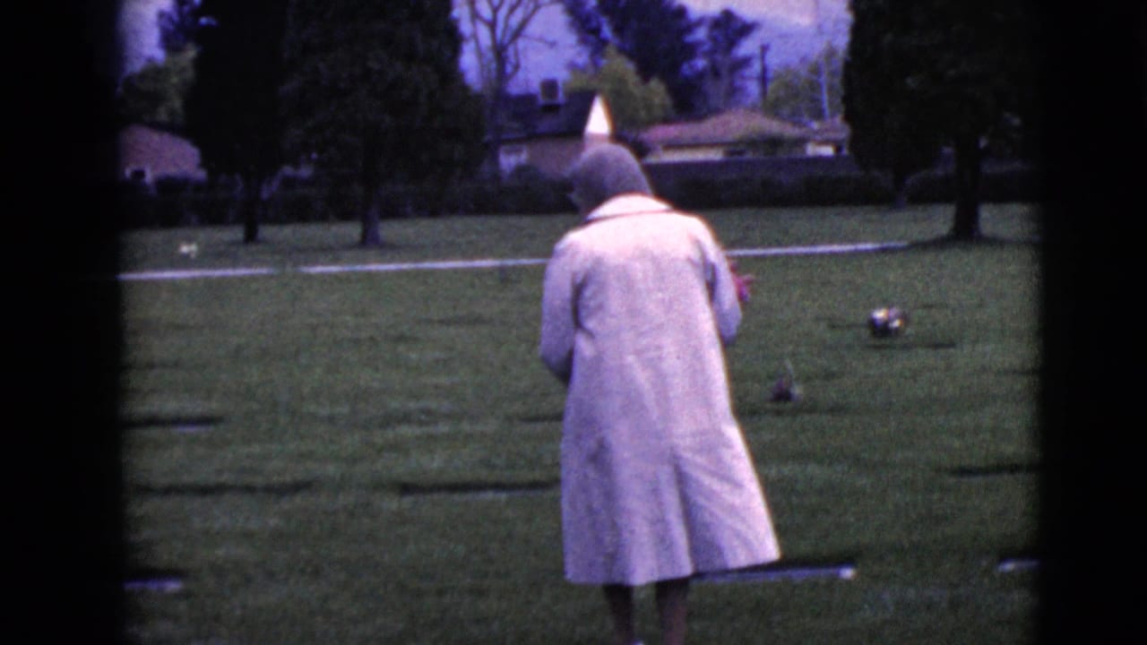 In the 1968 cemetery footage, the woman continues across the grass past flat grave markers and trees.