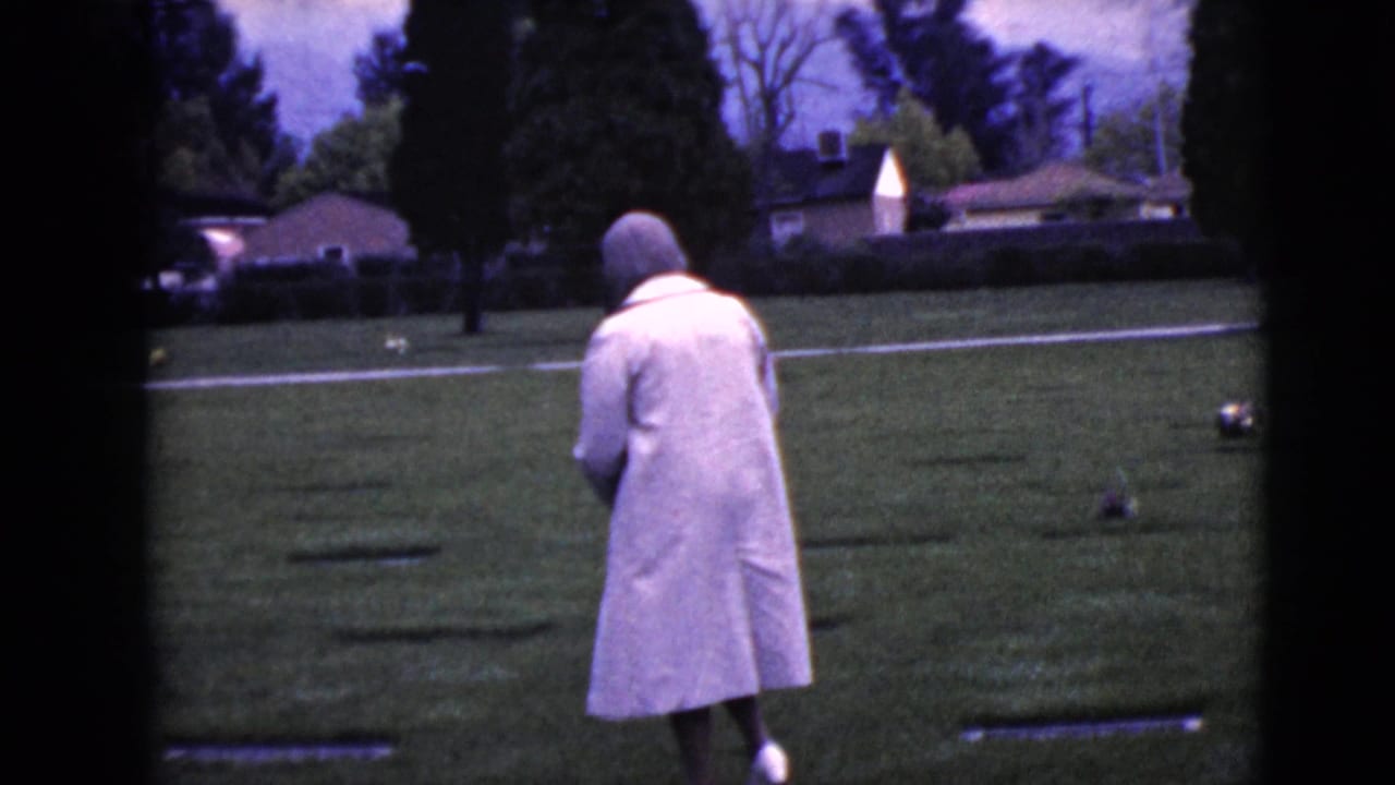 In Clarksdale, Arizona in 1968, an elderly woman in a pale coat and head covering walks through a cemetery lawn.