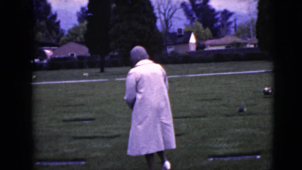 In Clarksdale, Arizona in 1968, an elderly woman in a pale coat and head covering walks through a cemetery lawn.