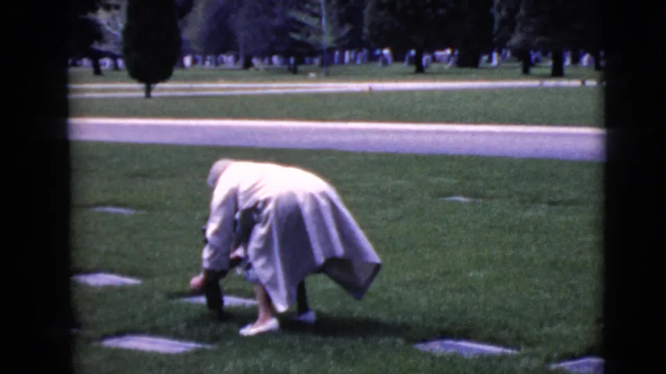 The final frame shows the woman still bent near the grave marker, framed by 8mm film borders and a broad cemetery lawn.