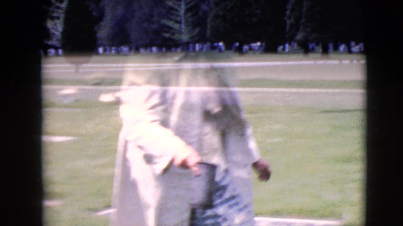 Blurred figure in a light coat stands on a cemetery lawn near grave markers.