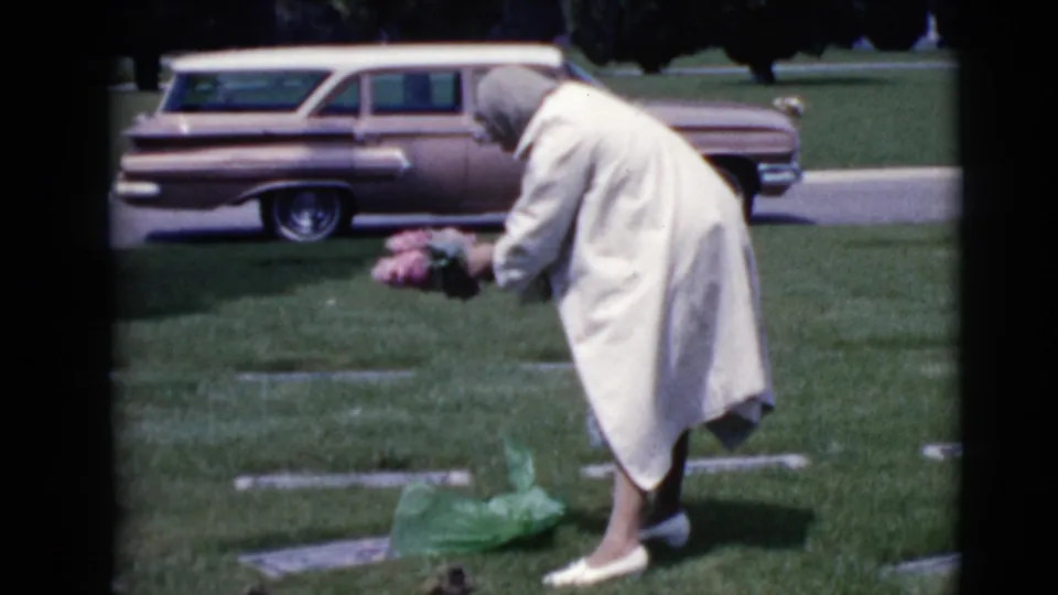 In the final frame, the woman reaches toward the grave marker with flowers, framed by the grassy cemetery and a vintage station wagon.