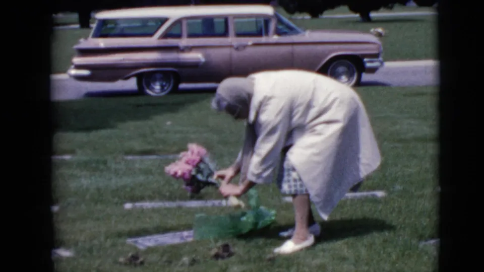 In the final frame, the woman bends toward the grave with flowers and wrapping visible, while a 1960s station wagon is parked behind her.