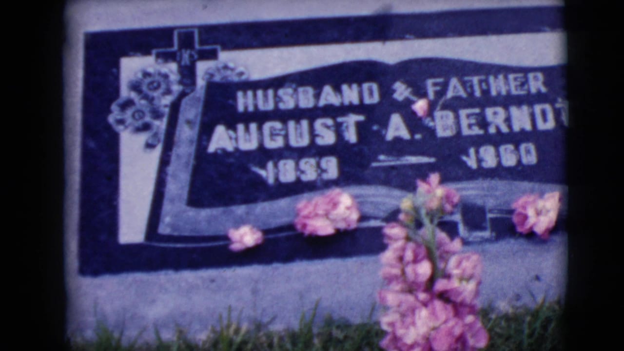 Flat grave marker for August A. Berndt with pink flowers and grass around it.
