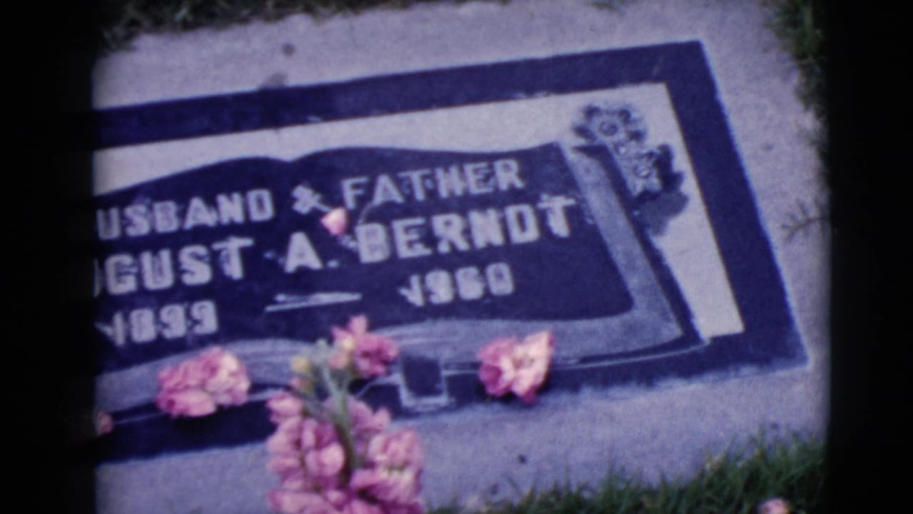 Closer tilted view of the same grave marker with flowers across the lower edge.