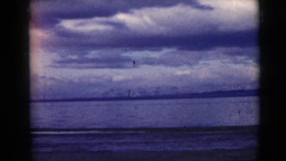 1968 8mm home-movie frame showing a wide water surface, low distant shore, and dense cloud cover with visible grain.