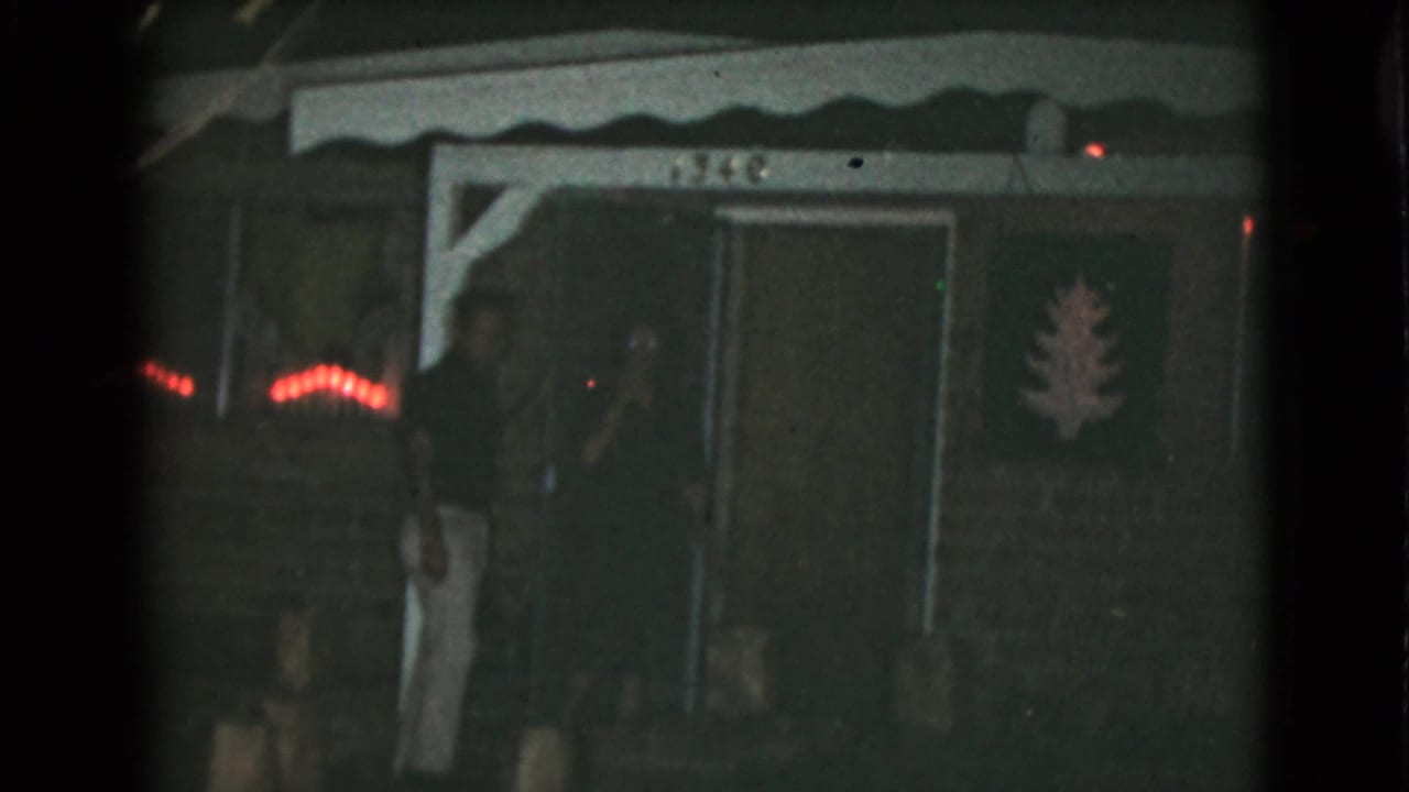 The couple remains near the doorway of a Clarksdale, Arizona home, with red string lights glowing beside the porch.