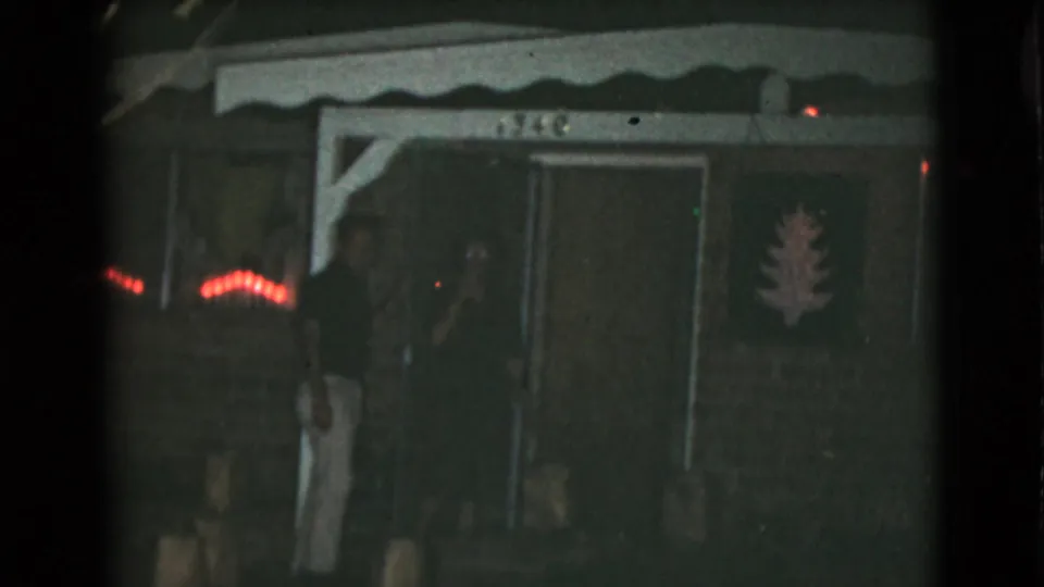 The couple remains near the doorway of a Clarksdale, Arizona home, with red string lights glowing beside the porch.