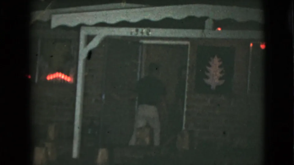 Near the end of the Clarksdale porch scene, a figure is low or bending by the entrance beneath the awning and house number.