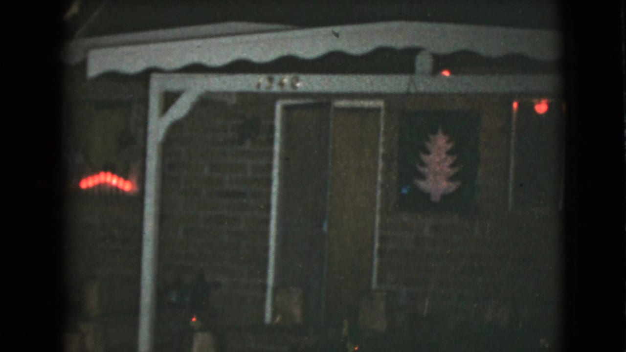 House front at night with dark doorway, red lights, and a tree-shaped wall decoration.