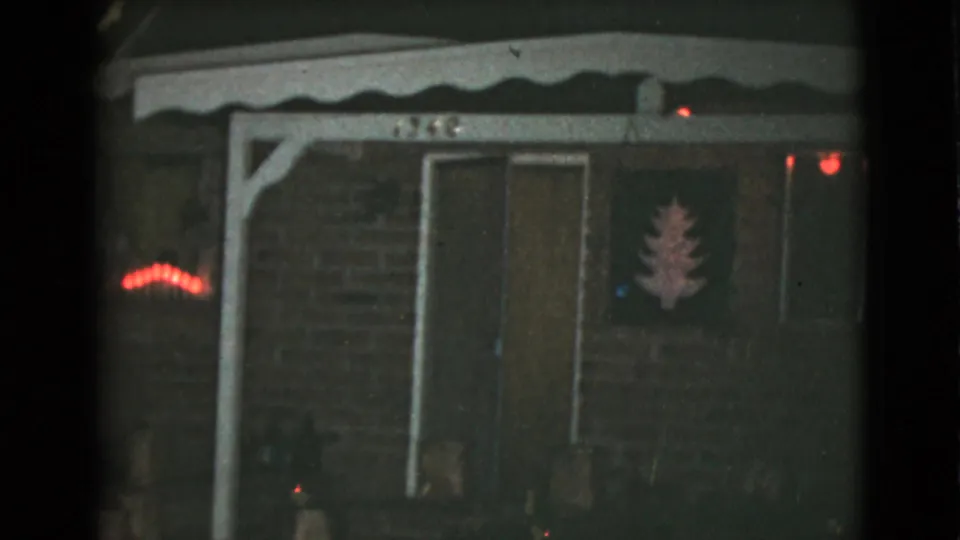 1968 8mm frame showing the Clarksdale house facade at night, including a doorway, porch trim, red lights, and tree-shaped decoration.